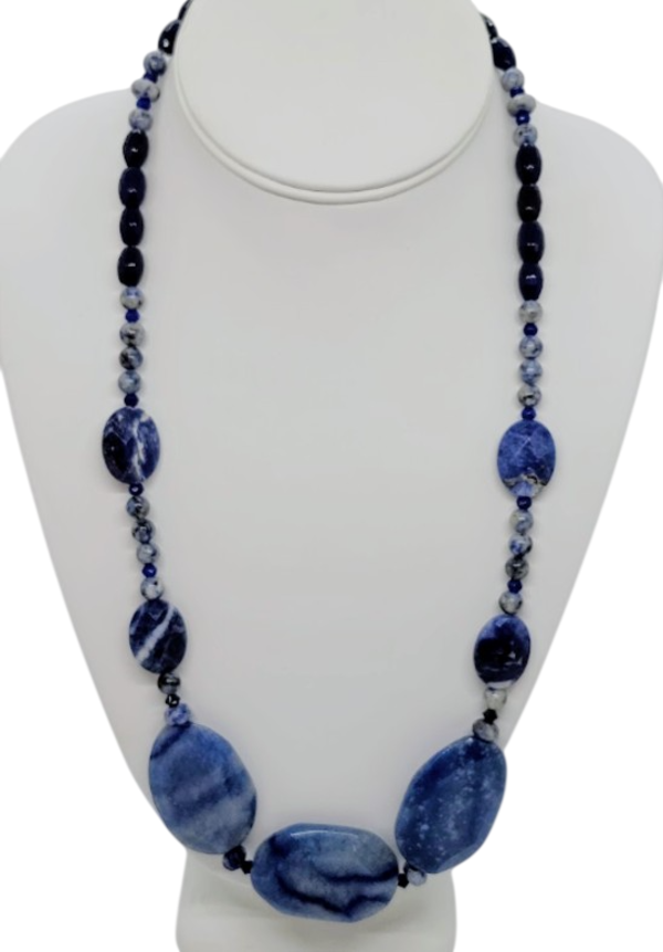 A long beaded necklace displayed on a white mannequin bust. The necklace features large oval navy blue and white marbled beads at the bottom, smaller oval blue marbled beads, and strands of dark blue, and white marbled beads.