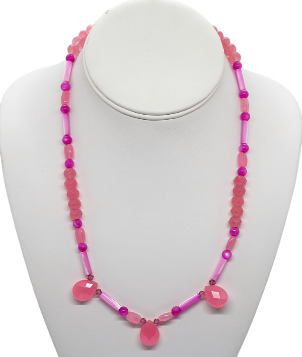 A pink and fuchsia beaded necklace with three teardrop-shaped pink beads hanging at the center front. The necklace is displayed on a white jewelry bust. The necklace is made up of semi-precious stones, mother-of-pearl, and crystals.