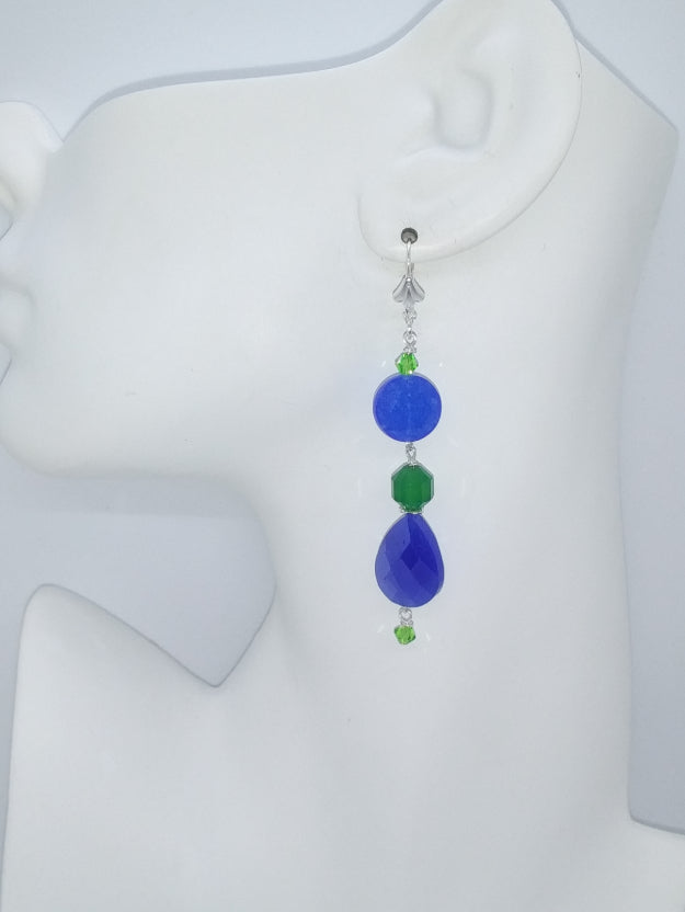 Royal blue and emerald green dangle earring with crystal accent hanging on a mannequin ear.