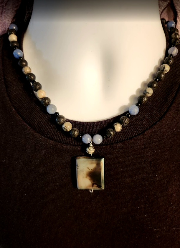 A blue, black and gray men's beaded necklace made with round  jade, lava rock, and zebra jasper stones and an agate pendant.