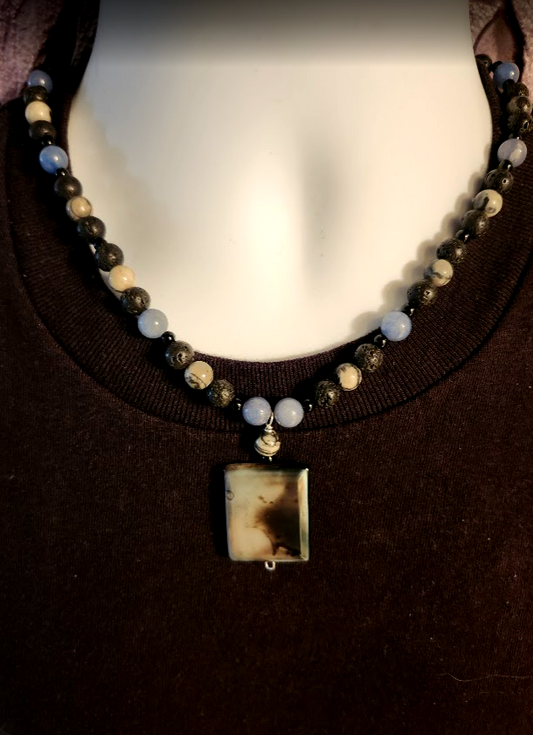 A blue, black and gray men's beaded necklace made with round  jade, lava rock, and zebra jasper stones and an agate pendant.