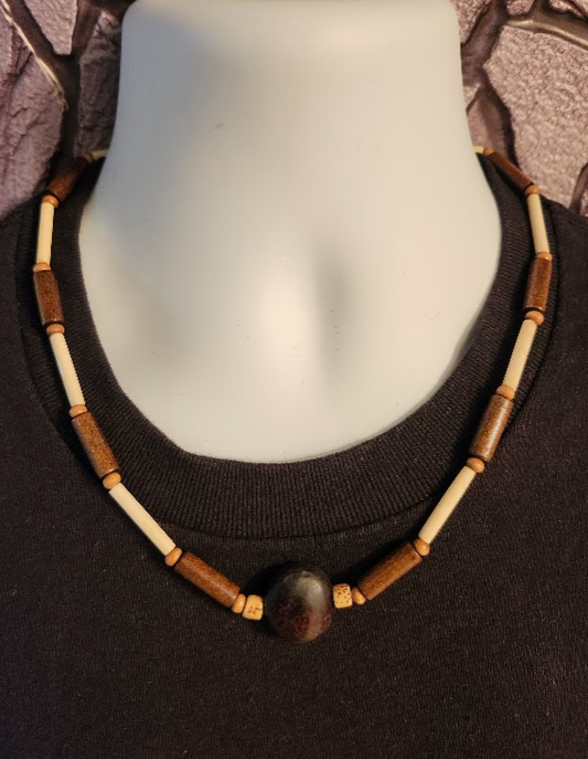 A brown , beige, and cream men's beaded necklace with wood and bone beads and a kola nut pendant.