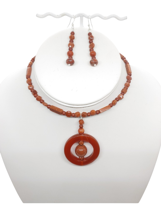 A jewelry set  that is made up of semi-precious stones, goldstone and carnelian, and features a  rust brown beaded choker-style necklace and matching drop earrings displayed on a white mannequin bust.   