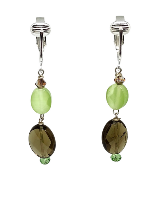 A pair of clip-on dangle earrings featuring a light green oval bead, a small faceted brown crystal, and a larger brown oval faceted bead with a tiny green accent bead at the bottom.