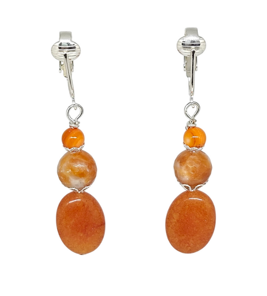 A pair of drop earrings featuring three stacked orange stone beads in oval and round shapes, suspended from silver-toned ear clips.