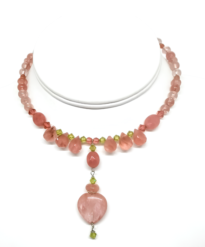 An expandable choker with cherry quartz beads, faceted jade-style beads and a drop pendant featuring a cherry quartz heart on a white mannequin