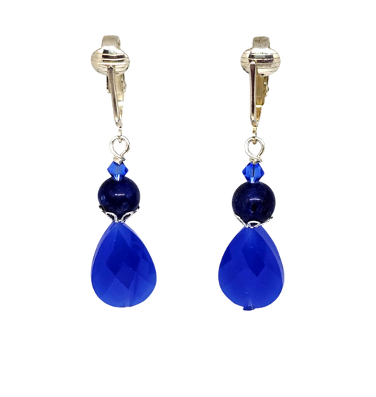 A pair of drop clip-on earrings with pierced-look ear clips and a small faceted blue crystal, a navy blue bead, and a large faceted royal blue teardrop bead, shown on a plain white background.