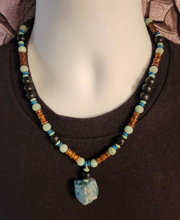 This is a teal, brown, aqua, and black men's beaded necklace with wood, bamboo and semi-precious stones, and it has a raw textured stone pendant.